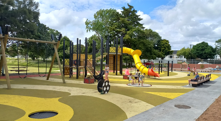 Riverhead War Memorial Park - A merry-go-round and play equipment leading up to a tall tunnel slide.