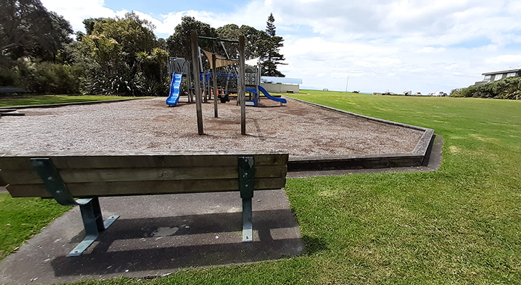Rothesay Bay Beach Reserve - Bench seat with the playground in the background.