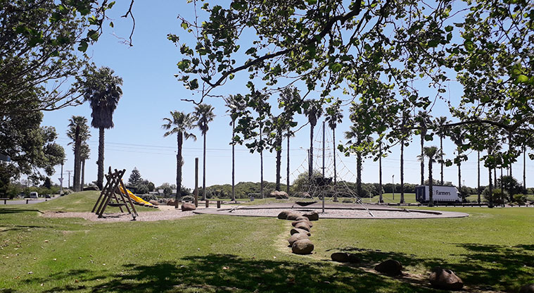 Seaside Park - Looking from under the trees to the playground with spider net, swings and double slide.