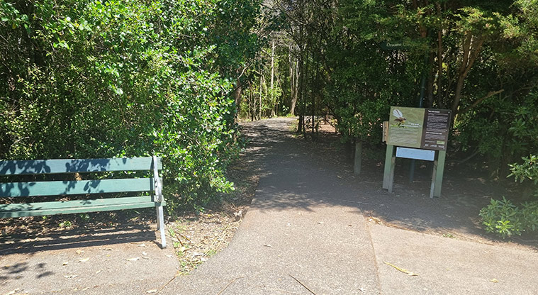 Shepherds Park – The entrance to the track through the bush with a bench seat on the left and an information sign on the right.