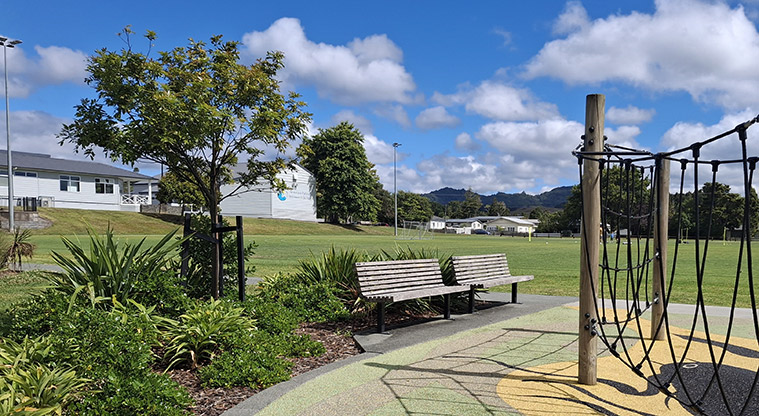 Shoesmith Domain Recreation Reserve - Two seats on the edge of the path with part of the playground and the sports fields in the background.