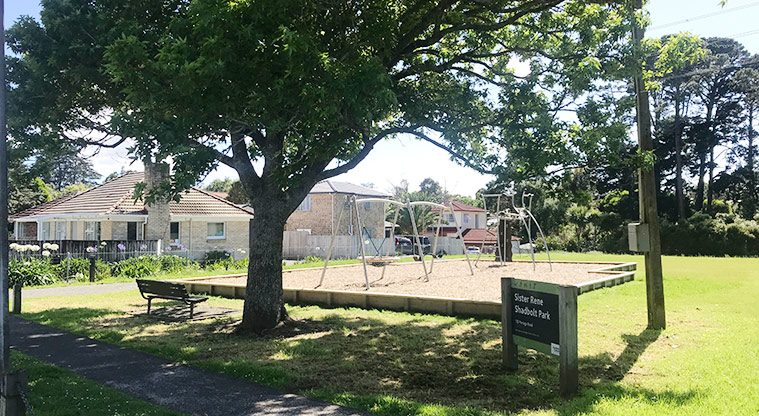Sister Rene Shadbolt Park - Looking under the trees at the park entrance sign with the playground and open space in the background.