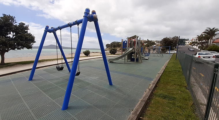 St Heliers Bay Beach Reserve - Set of two swings (western end of the playground) with the rest of the playground and Rangitoto Island in the background.