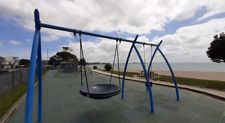St Heliers Bay Beach Reserve - Swing set with a basket swing at the eastern end of the playground with the beach in the background.