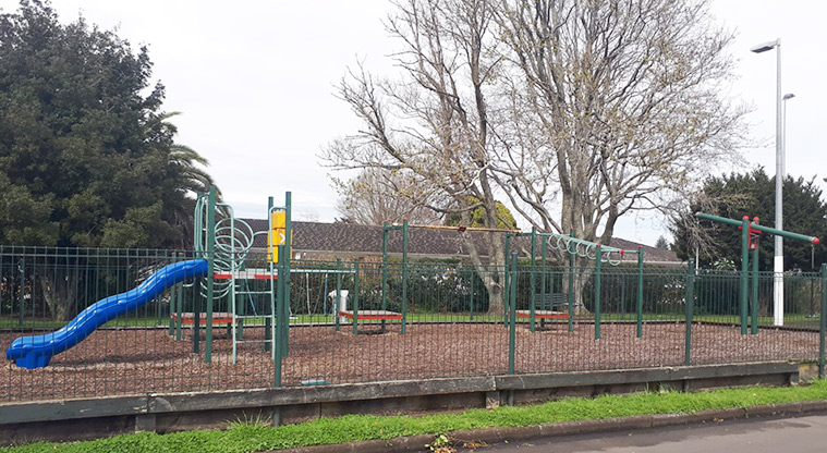 Stadium Reserve - Playground with various platforms, climbing and swinging equipment and a slide behind a tall green fence.