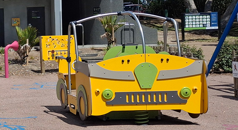 Takapuna Beach Reserve - Yellow and green rocking truck with a sensory board and the toilets in the background.