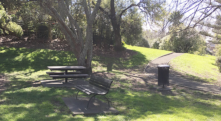 Taumata Reserve - A seat and picnic table under the trees by the playground. Photo credit: S Hulse.