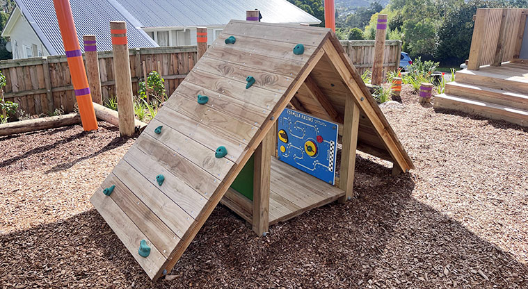 Taurus Crescent Reserve - Low wooden cubby house with a climbable roof and interactive play boards attached to the inside walls.