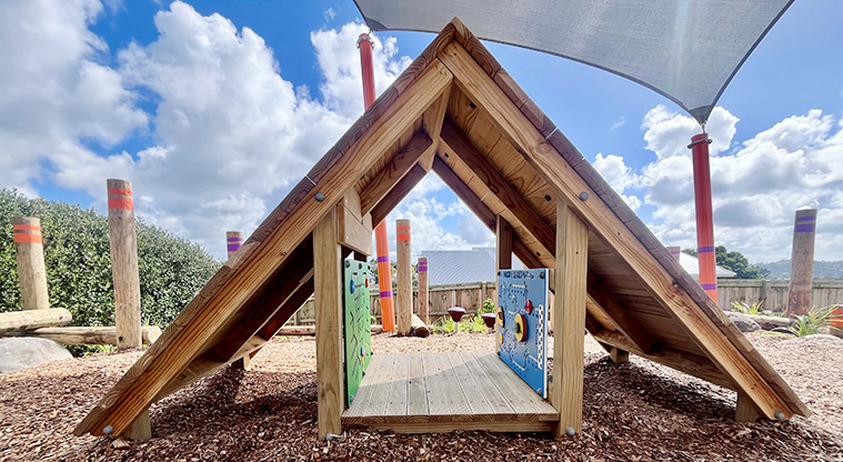 Taurus Crescent Reserve - Low wooden cubby house with a climbable roof and interactive play boards attached to the inside walls.