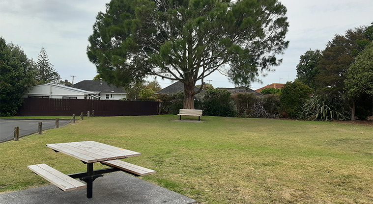 Te Atatū Peninsula Park - Picnic table and seating with a section of the large car park on the left and trees in the background. Photo credit: Tracey Hodder.