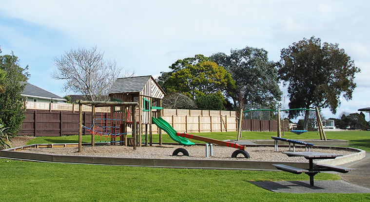 Te Atatu Peninsula Park - The playground on a bark base with the path on the right and a picnic table in the foreground.