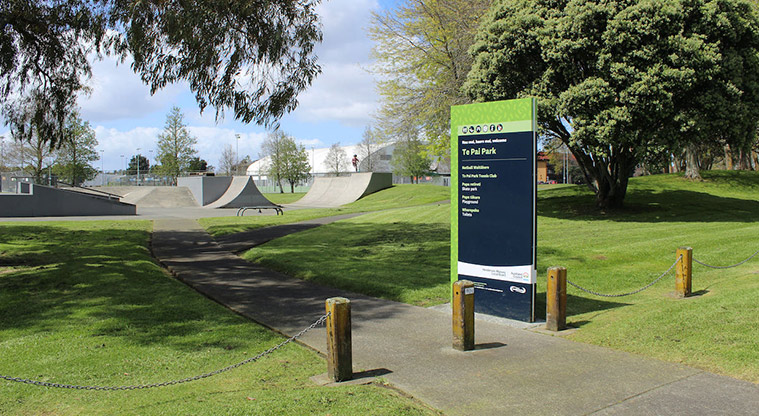 Te Pai Park - Sign at the pedestrian entrance off Lincoln Road, with open space, the skate park and trees in the background.