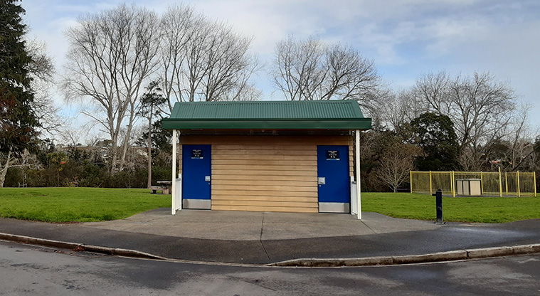 Tūī Glen Reserve - Two accessible toilets with a fenced barbecue to the right, and open space and trees on the left.