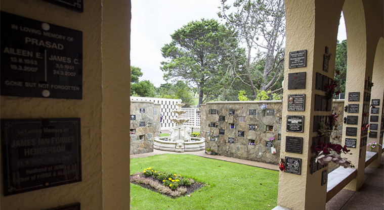 Waikumete Cemetery – Looking through a window to the Columbarium Wall with plaques showing where urns have been placed in each niche in the wall.