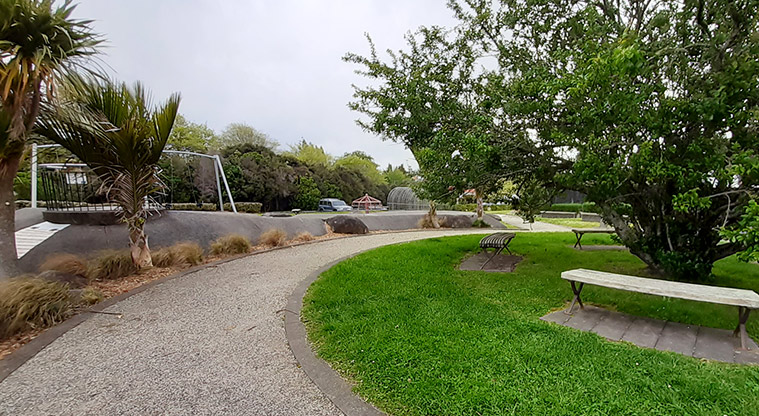 Wainoni Park North - Path with the playground on the left, and seats under a large tree on the right.