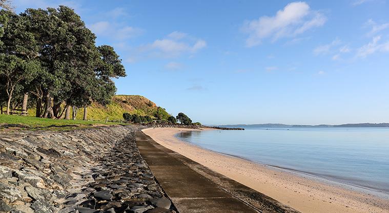 Waiomanu Reserve - Looking along the beach and a section of the rock wall and concrete path.