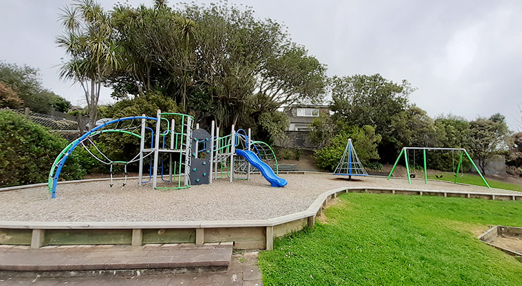 Swainston Reserve - Climbing net and wall, colourful play structure, swings and open space with trees.