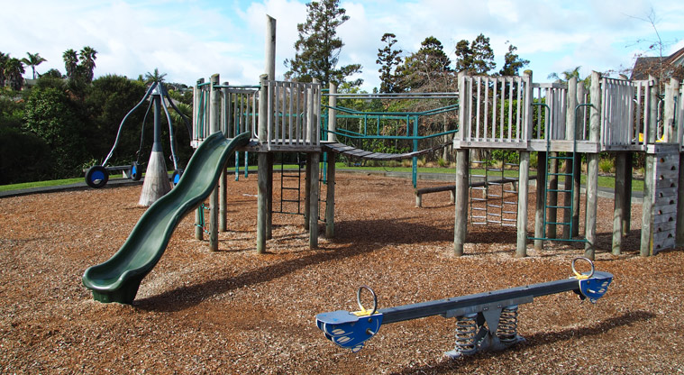 Xena Park - Blue seesaw, a slide with climbing equipment and a swinging wooden bridge, and a spinning pole towards the back. Photo credit: Tracey Hodder.