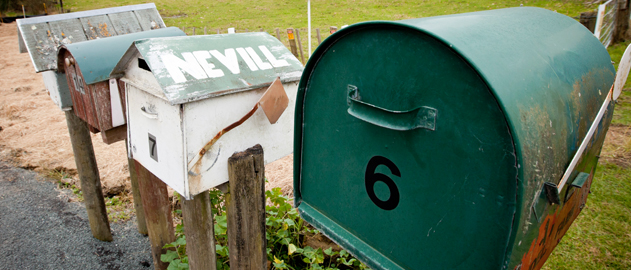 A row of different kinds of letterboxes in a rural area.