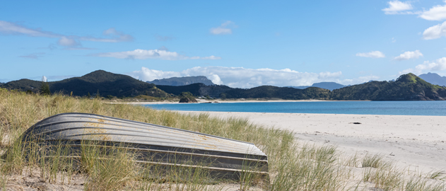 Medlands Beach in Aotea showing an upturned boat on white sand near the blue sea.