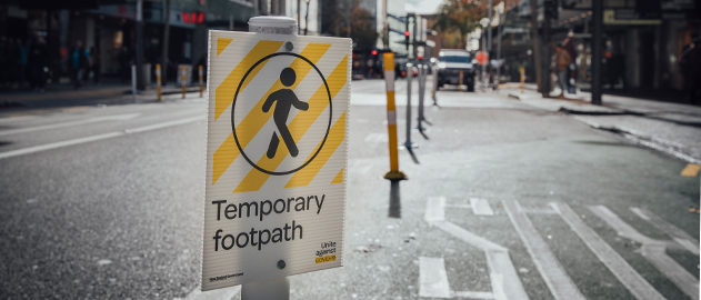 Photo of a COVID-19 temporary footpath sign and road.