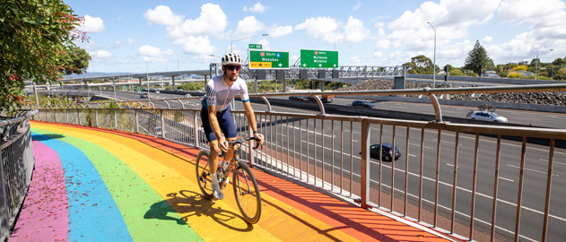 A man cycling along a rainbow-coloured path with a motorway in the background.