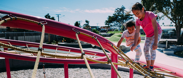 Two young girls climbing over a rope net at a playground.