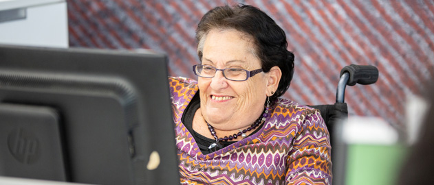 A woman in her wheelchair smiling at a laptop.