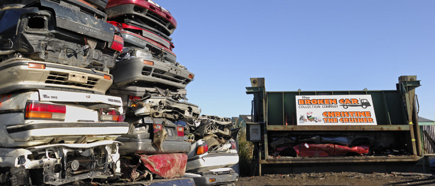 Piles of crushed cars next to a car crushing machine. 