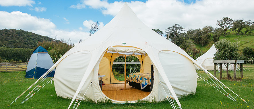Large white tent on grass with trees and hills in the background