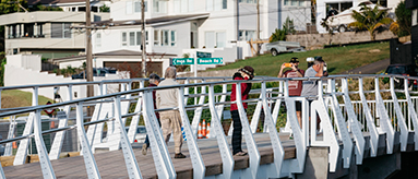 Photo showing a number of people walking across a bridge towards a street.