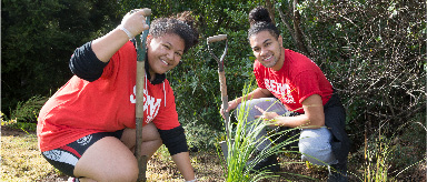 Photograph of two people at the Otara Creek planting native grass.