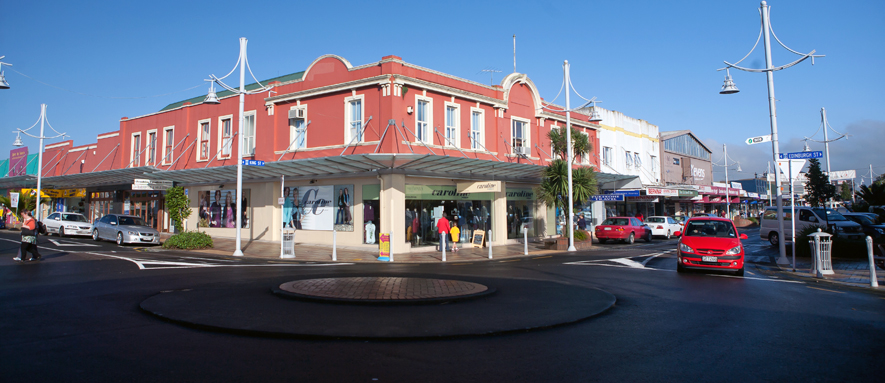 Photograph of the intersection of King Street and Edinburgh street, pedestrians are walking along the revitalised pathways next to the shops and a red car is waiting to use the round about