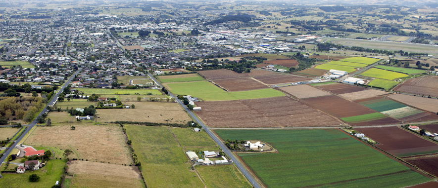 Photograph of Pukekohe from the air that shows some of the rural land and homes around the high density residential areas and town