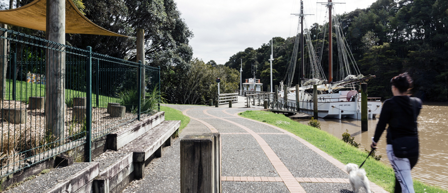 Photograph of a woman walking her dog along the boardwalk next to the Mahurangi river.
