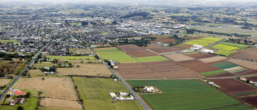 Photograph of Pukekohe from the air that shows some of the rural land and homes around the high density residential areas and town