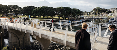 Photo of a bridge with several people walking over it, and two men looking on.