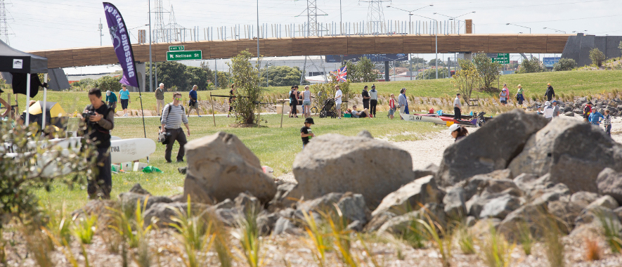 Aucklanders enjoying a parkland with decorative rocks in the foreground and a bridge in the background.