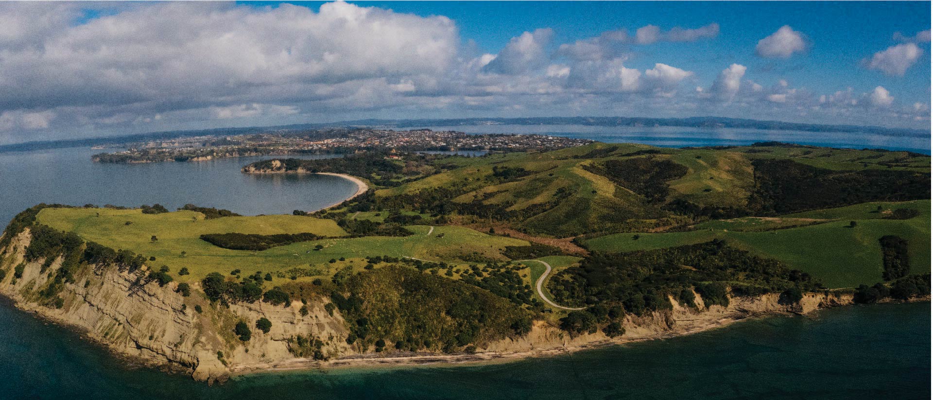 Aerial view of Shakespear Regional Park, Whangaparaoa Peninsula, that shows rolling hills and Pink Beach.