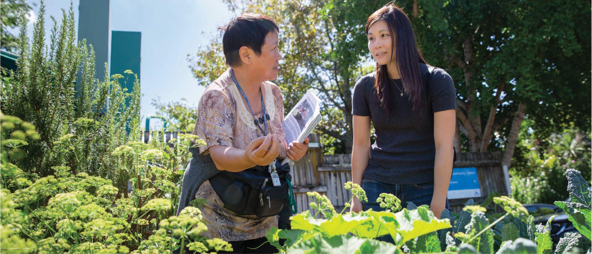 Two people in a community garden surrounded by vegetables and herbs.