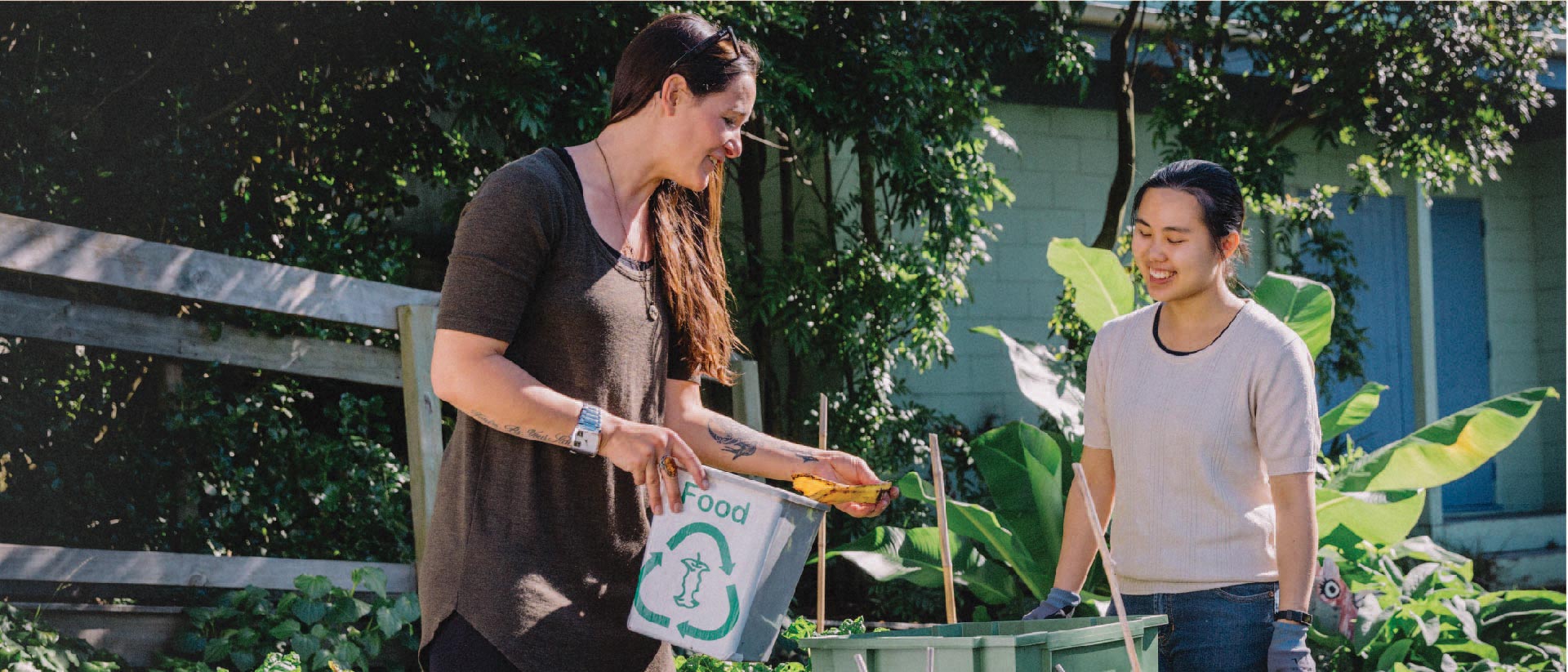Two people in a community garden adding food scraps to a worm farm