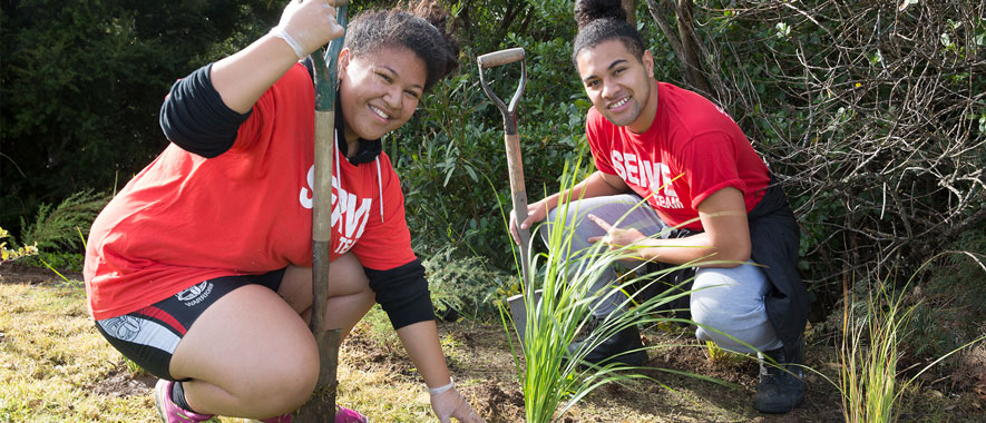 Two young adults planting flax in a grassy area.