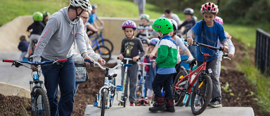 Lots of children riding their bicycles over the humps in the track at the opening of the Grey Lynn Pump Track