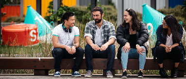 Photograph of four people sitting on bench chatting
