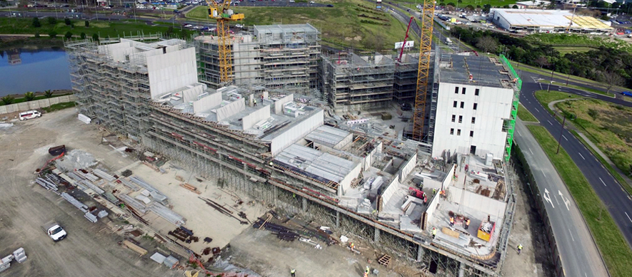 A development site in Auckland. A number of apartments are in the early stages of construction, with scaffolding surrounding them and cranes on site.